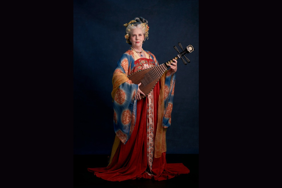 Full Tang stype empress with hair styling, jewelry wearing red brocade, blue and yellow layered sleeves while playing the lute 