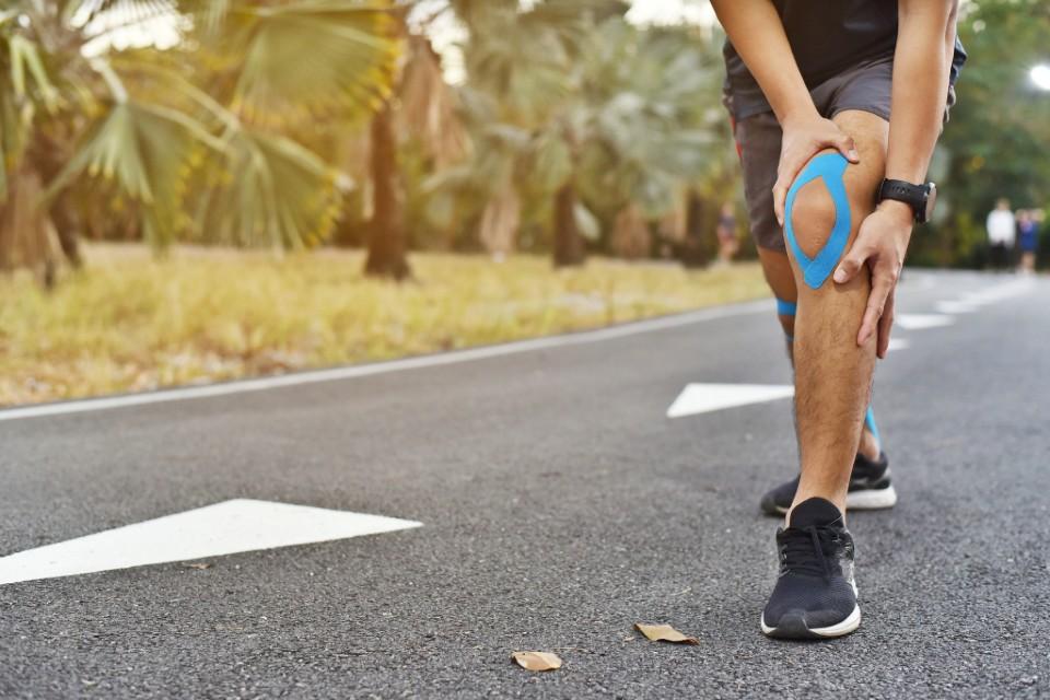 runner-holding-front-of-knee-with-kinesiology-tape-showing-symptoms-of-patellofemoral-pain-syndrome